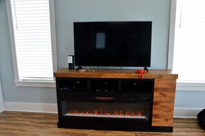 A wooden entertainment center with a flat-screen TV, a fireplace, and a small shelf with a toy. - Stunning! 4BR/3Ba - sleeps 10 - Swim Spa, Elevator and Pets Welcome (Carolina Beach)
