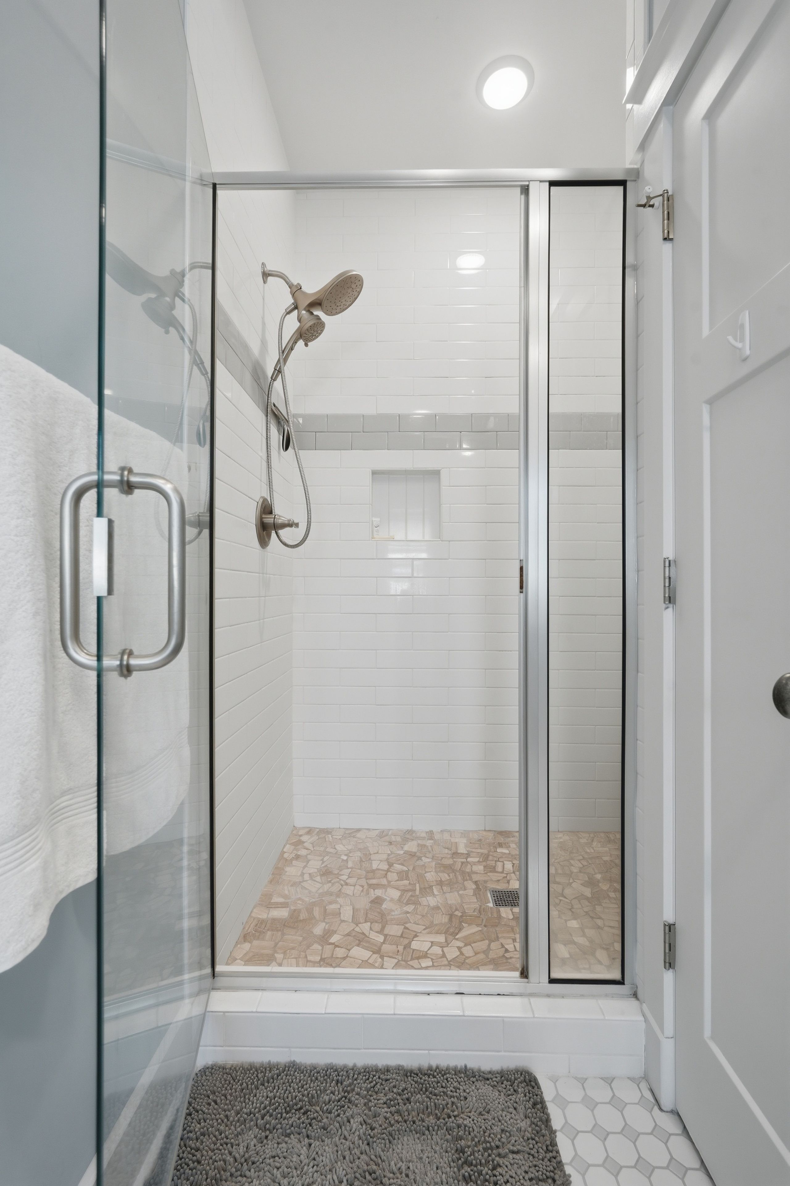 A glass-enclosed shower with a handheld showerhead and a handheld shower attachment.