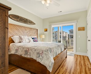 A bedroom with a wooden headboard, a bed with a quilt, a ceiling fan, and a view of a balcony with houses. - Stunning! 4BR/3Ba - sleeps 10 - Swim Spa, Elevator and Pets Welcome (Carolina Beach)