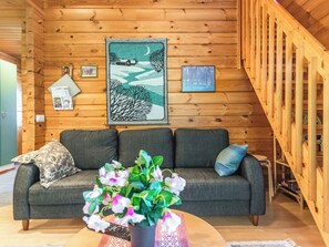L’intérieur d’un chalet chaleureux, avec un mur en bois, un canapé gris, un coussin bleu et un tableau représentant un paysage, encadré.