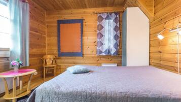 A cozy room with a bed, a chair, a table with a vase, and a window with curtains.