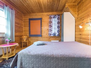A cozy room with a bed, a chair, a table with a vase, and a window with curtains.