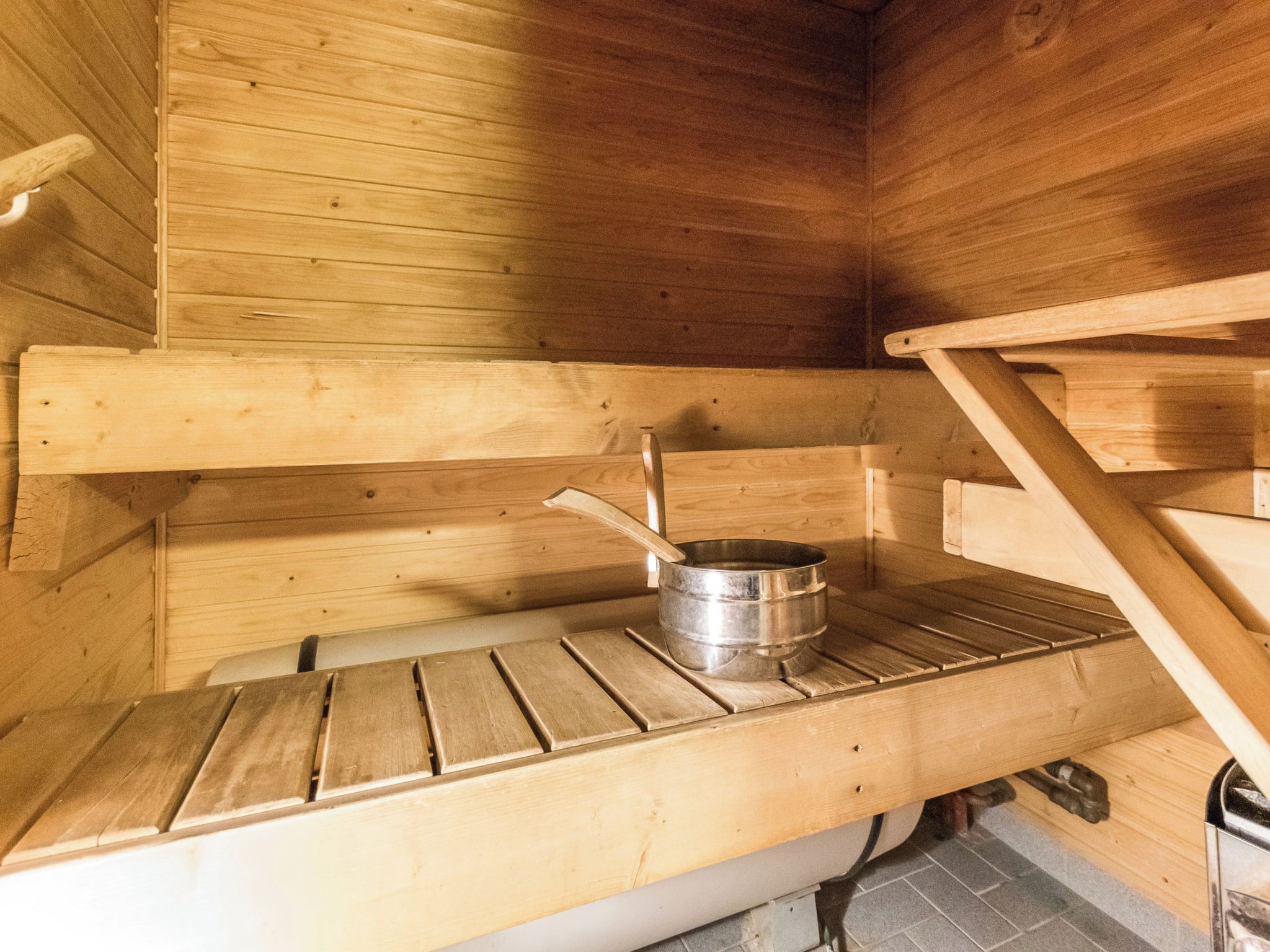 A sauna with wooden benches, a metal container, and a wooden shelf.