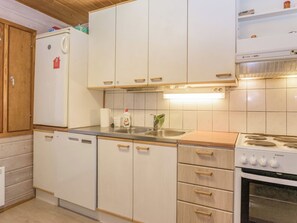 A compact kitchen with white cabinets, a built-in dishwasher, a stove, and a sink. - Iltarusko by Interhome (Savonlinna)
