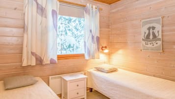 A cozy cabin room with two beds, a nightstand, a window with curtains, and a wall-mounted lamp.