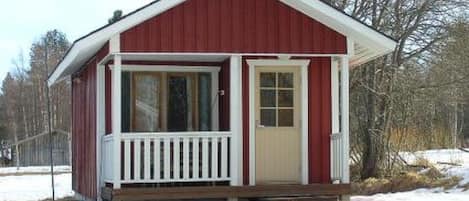 A small, single-story red cabin with a white porch and a door.