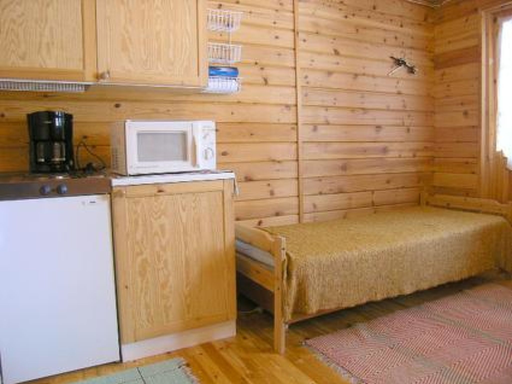 Ein kleines Zimmer im Blockhausstil mit Küchenzeile, einem Bett und einer Holzwand.