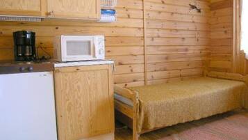 A small cabin-style room with a kitchenette, a bed, and a wooden wall.