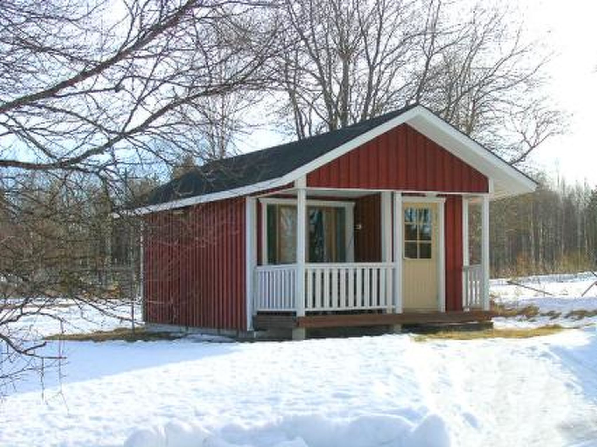 A small, single-story cabin with a red exterior and white trim, featuring a porch with a railing.