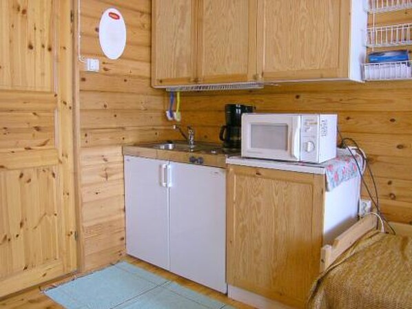 Cocina compacta con armarios de madera, un refrigerador blanco, un microondas y una cafetera.