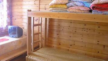 A wooden cabin room with bunk beds, a television, and a window with curtains.