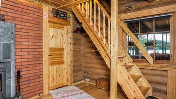 L’intérieur d’un chalet en bois, avec une cheminée, un escalier en bois et une fenêtre donnant sur la verdure.