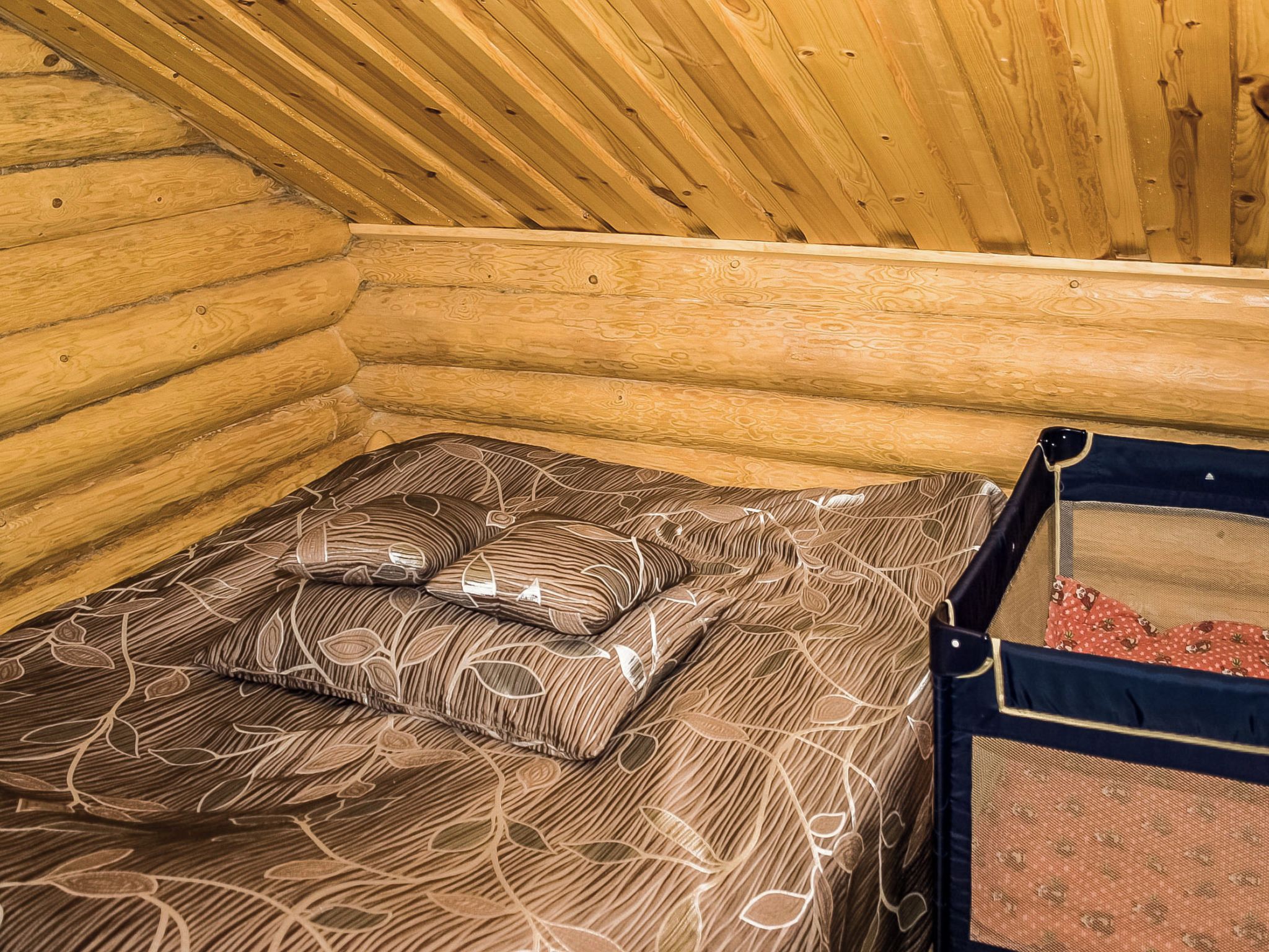 A wooden cabin interior with a bed, pillows, and a small enclosed area with a mesh door.