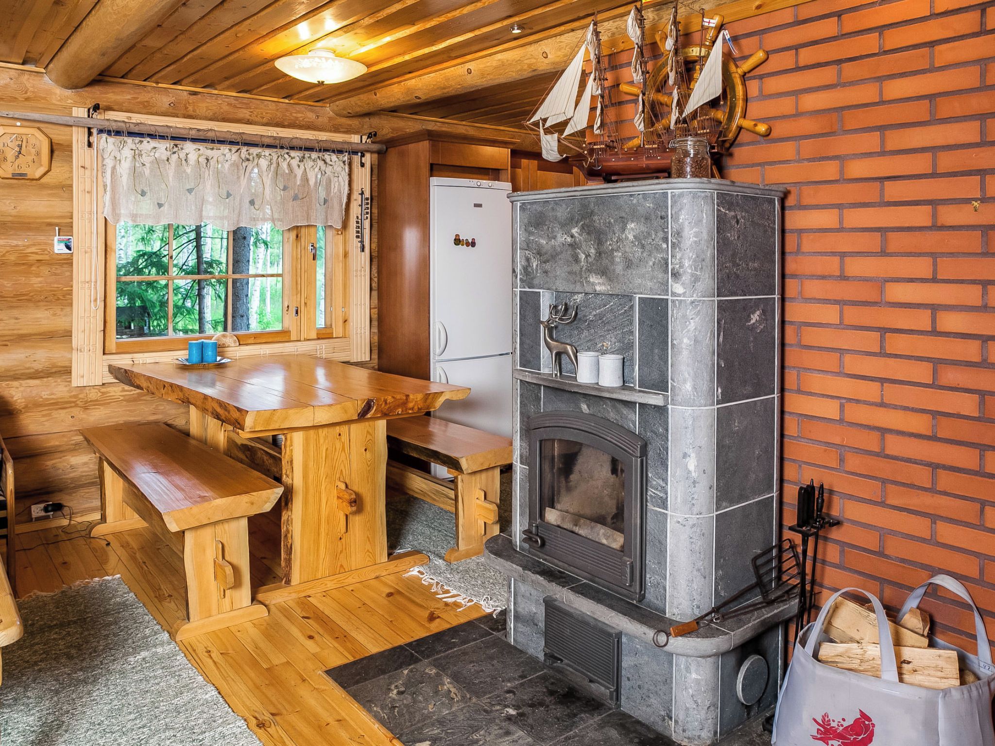 A rustic cabin interior with a wooden dining table, bench, and a stone fireplace.