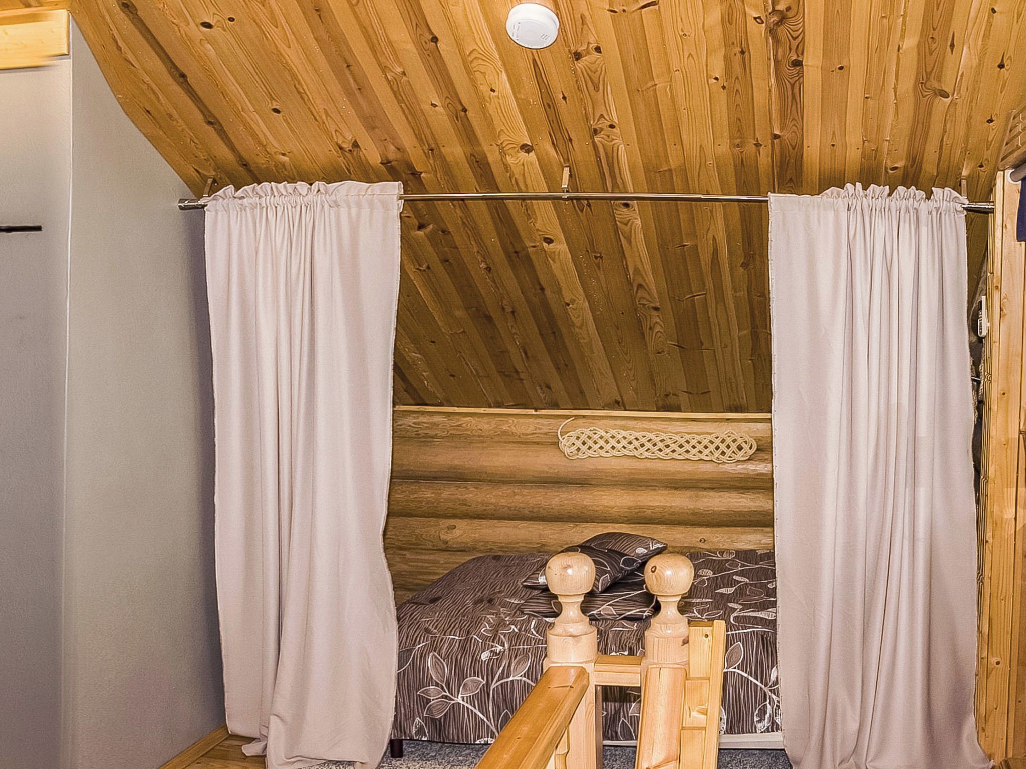 A cozy log cabin bedroom with a wooden ceiling, a bed with a floral-patterned bedspread, and a wooden headboard.