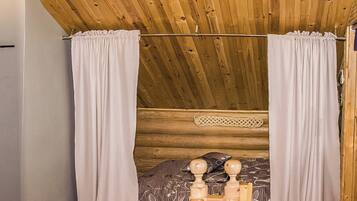 Ein gemütliches Schlafzimmer in einer Blockhütte mit Holzbalkendecke, einem Bett mit blumigem Überwurf und einem Holz-Kopfteil.