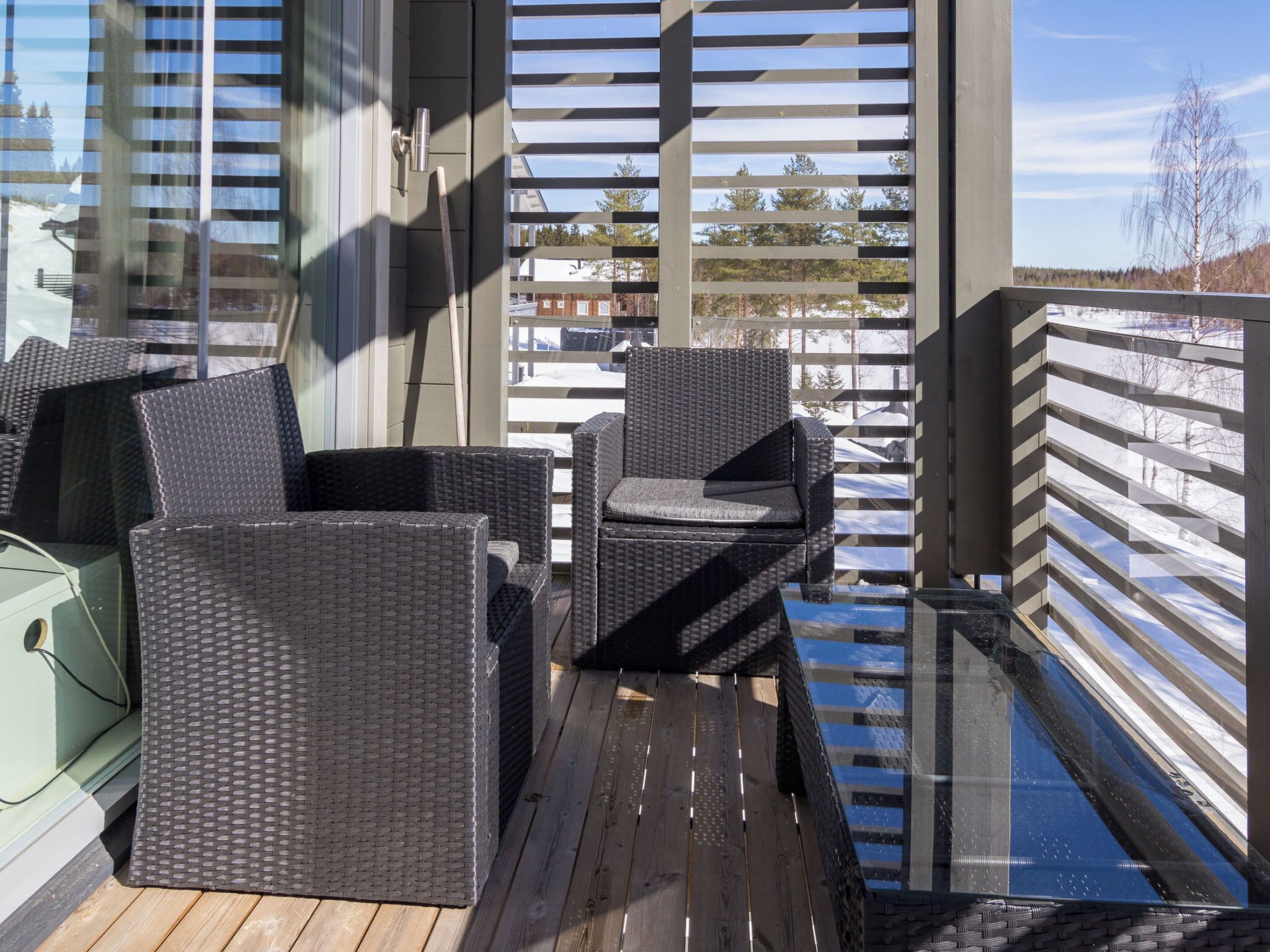 A balcony with wicker furniture, a glass door, and a view of a snowy landscape.