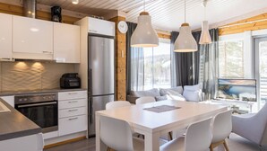 Una cocina moderna con armarios blancos, un refrigerador de acero inoxidable y un comedor con mesa y sillas blancas.