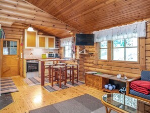 Hirsihirrestä rakennetun mökin sisätilat, joihin kuuluu keittiö, ruokailutila ja olohuone.