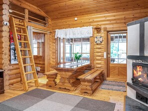 Hirsihirrestä rakennetun mökin sisätilat: puinen pöytä, takka, tikapuut ja ikkuna, jossa on verhot.
