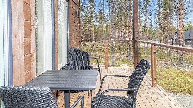 Een houten terras met tafel en stoelen, met uitzicht op een bebost gebied.