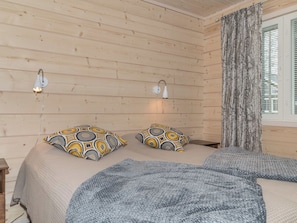 Una habitación de madera con una cama, dos lámparas de pared y un ventanal con cortinas.
