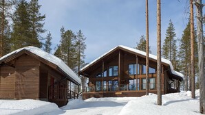 Een chalet met een groot raam, omringd door sneeuw en hoge bomen.