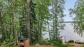 Un chalet rustique aux murs de briques, entouré d’une forêt dense et bordé d’un lac.