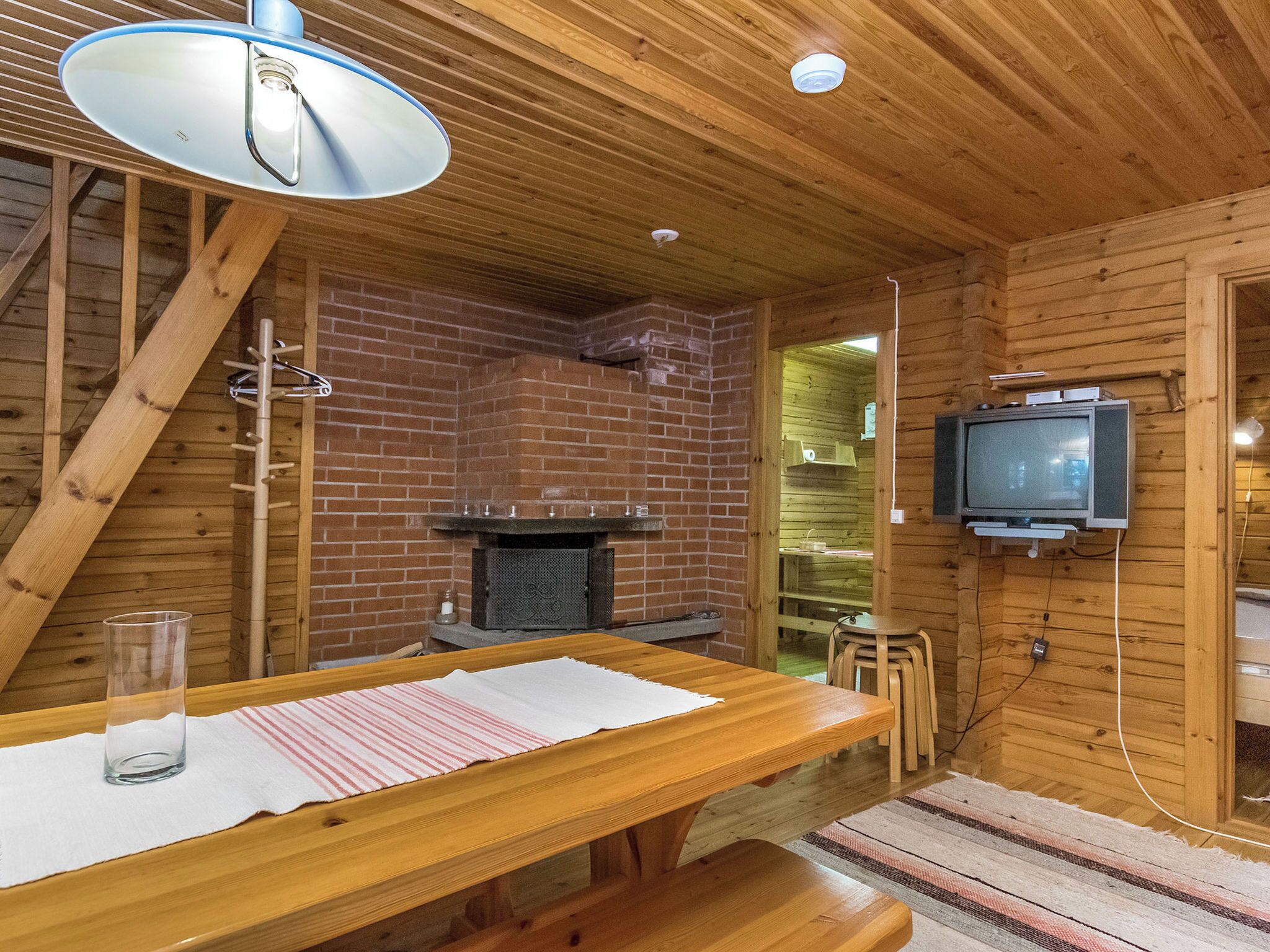 Een houten interieur met een open haard van baksteen, een aan de muur bevestigde televisie en een houten tafel met een glazen vaas.