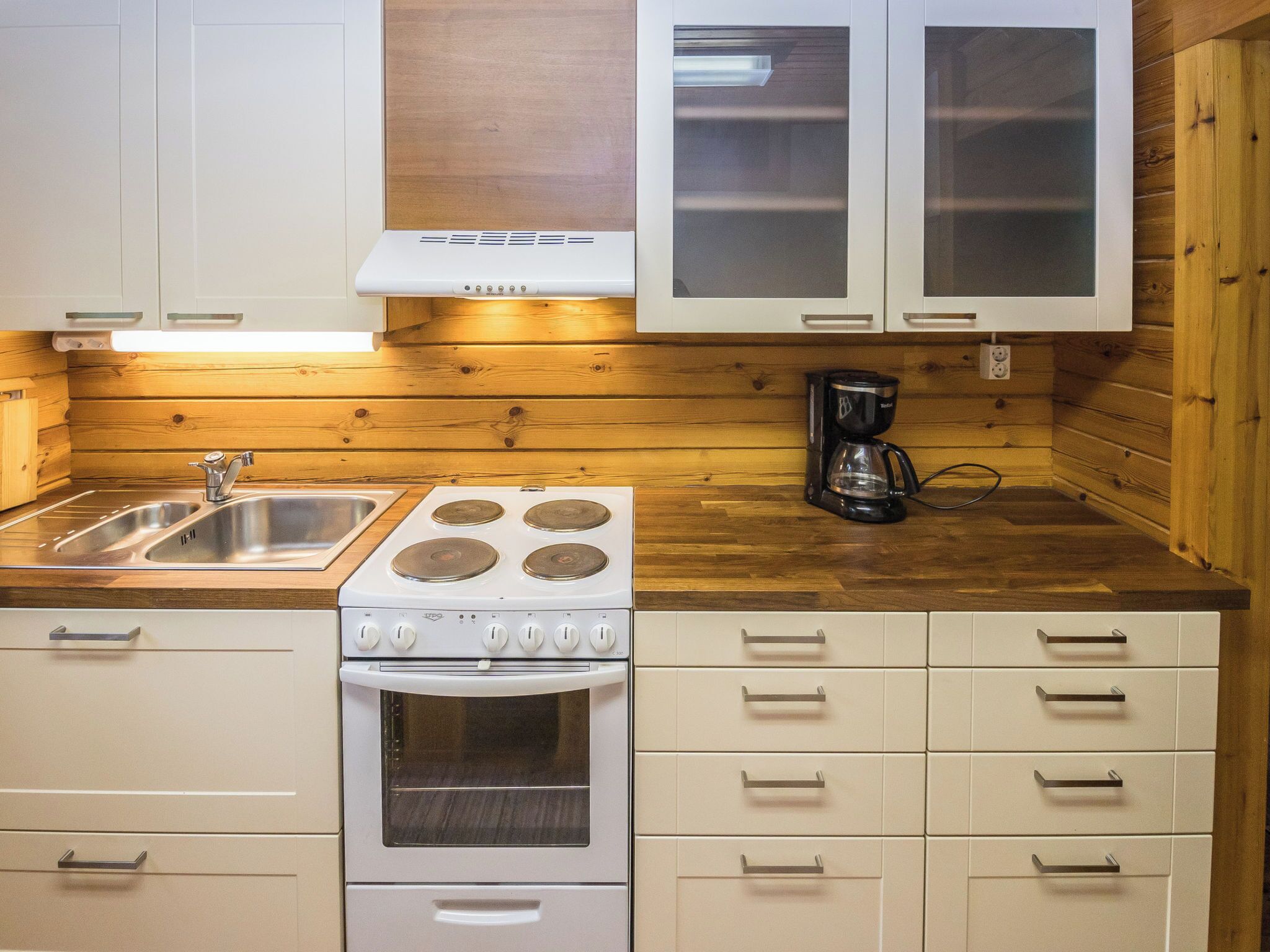 A compact kitchen with white cabinets, a stove, an oven, a sink, and a coffee maker.