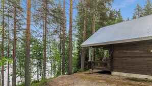 Une cabane avec un toit en métal, une terrasse en bois et une vue sur une zone boisée.