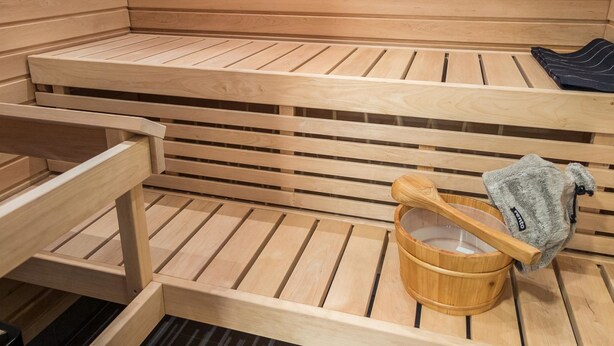 Een houten sauna met banken en een houten emmer met een schuimspaan.