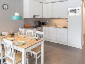 Een moderne keuken met witte kasten, een inbouwmagnetron en een eethoek met een houten tafel en witte stoelen.