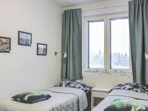 Une chambre avec deux lits, une fenêtre avec des rideaux et trois tableaux encadrés accrochés au mur.