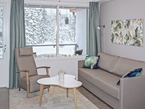 Een moderne woonkamer met een bank, twee stoelen, een salontafel en uitzicht op met sneeuw bedekte bomen door grote ramen.