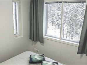 Une chambre avec un lit, une fenêtre avec des rideaux et une vue sur des arbres couverts de neige.