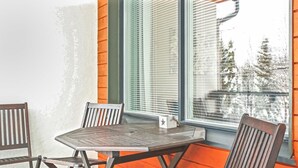 Een zithoek met een metalen tafel en twee houten stoelen, een klein wit doosje met een ster, en een raam met luxaflex.
