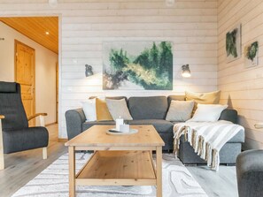 En hyggelig stue med et træsofabord, en grå sofa og et stort abstrakt maleri på væggen.