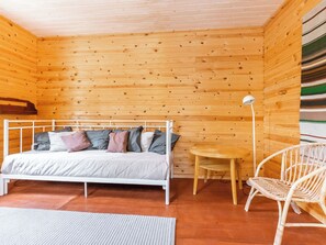 A wooden cabin room with a bed, a small table, a chair, and a lamp.