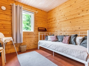 A wooden cabin room with a bed, a window with curtains, a small table, and a basket.