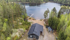 Una cabana a la vora d'un llac amb un moll, envoltada per un bosc dens.