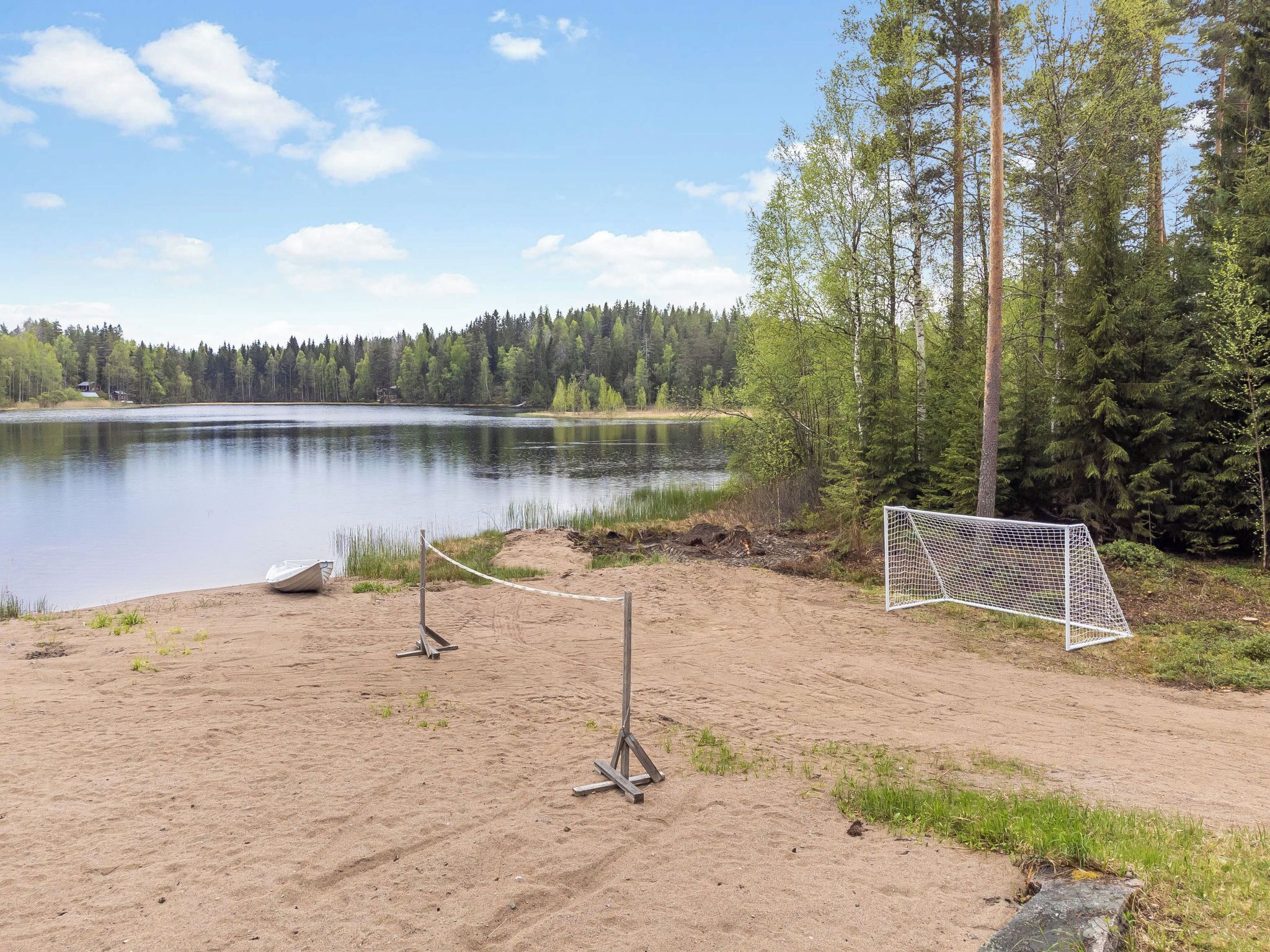 A sandy beach with a goalpost, a calm lake, and a forest in the background.