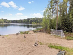 A sandy beach with a goalpost, a calm lake, and a forest in the background. - Kalliolaakso by Interhome (Ikaalinen)