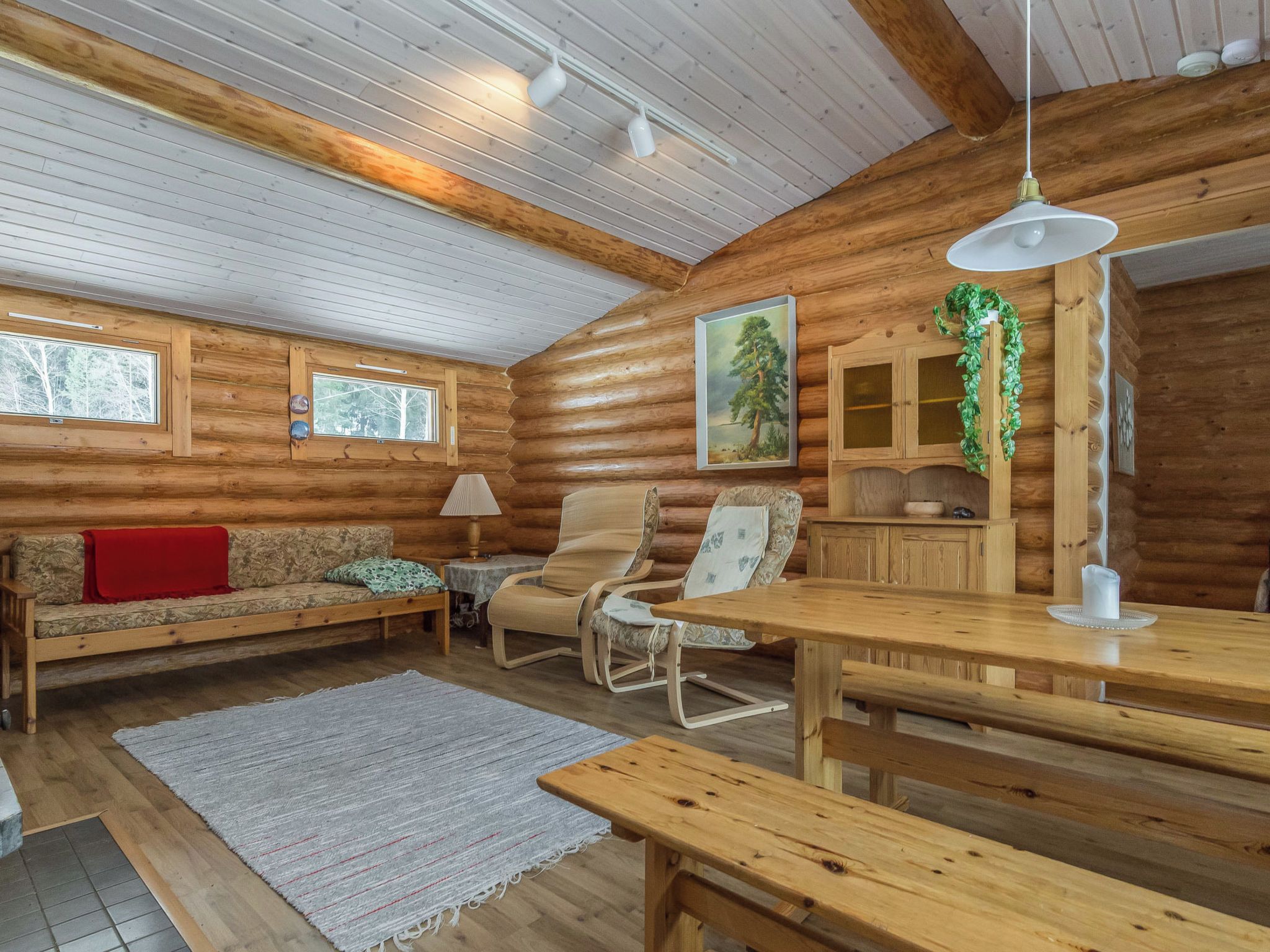 A cozy cabin interior with a wooden floor, a sofa, a chair, a table, and a hanging light fixture.