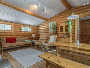 L’intérieur d’un chalet accueillant, avec un plancher en bois, un canapé, un fauteuil, une table et un luminaire suspendu.