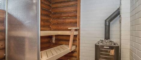 A sauna room with wooden benches, a bench seat, and a wood-burning stove.