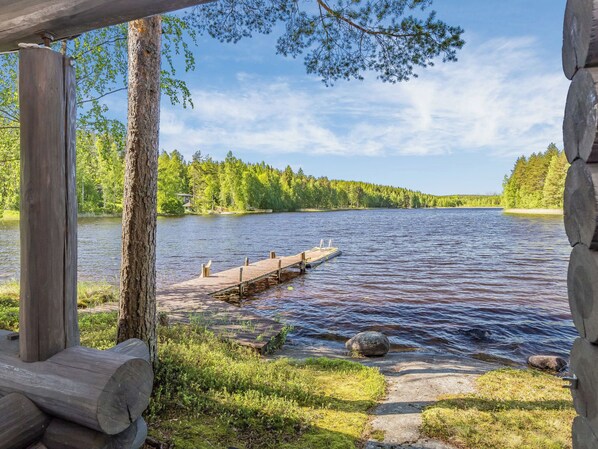 A wooden dock extending into a calm lake, surrounded by lush greenery and a clear sky.