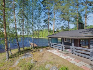A cabin with a deck overlooking a lake, surrounded by trees.