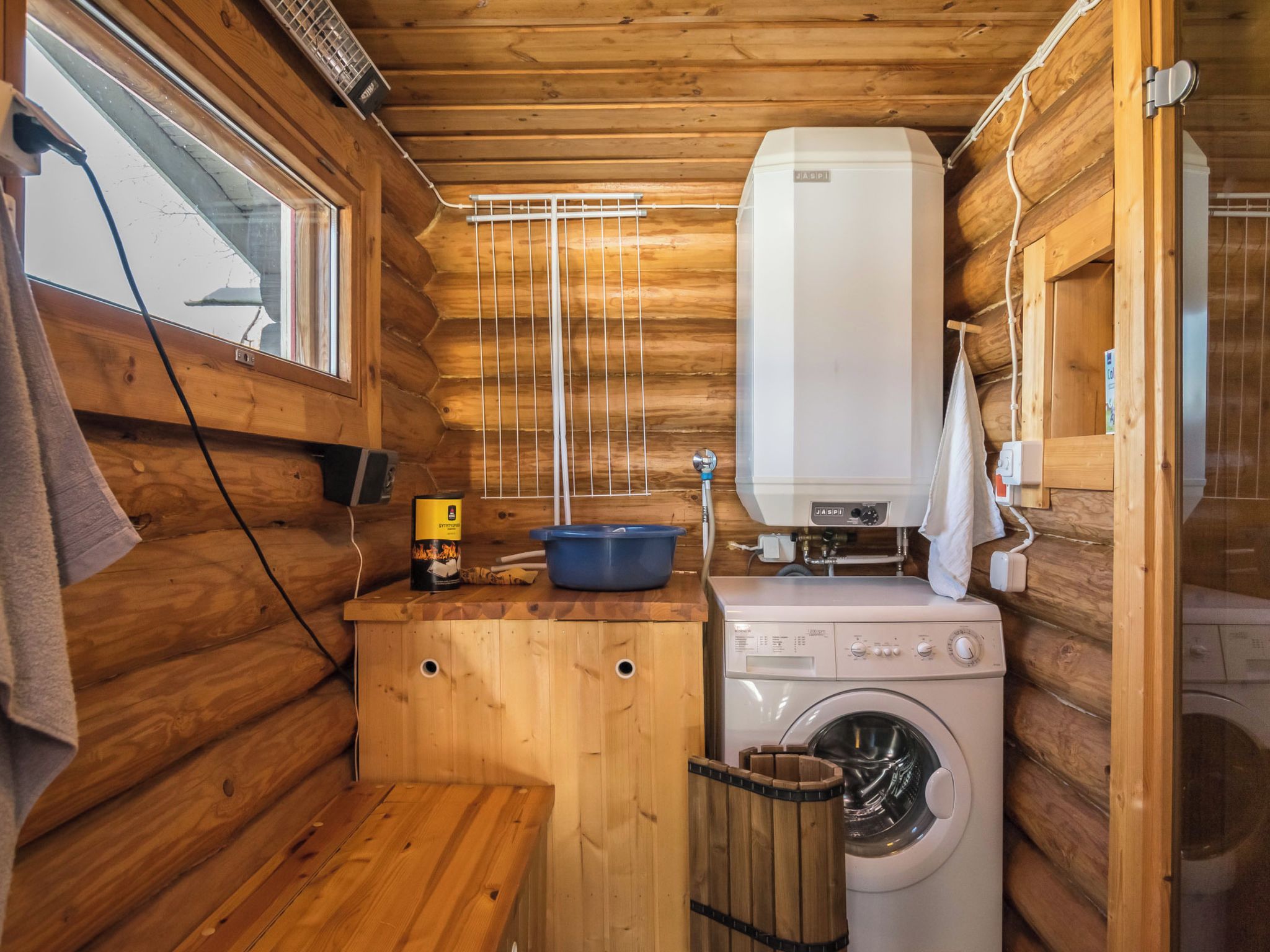 A compact wooden cabin with a washing machine, a blue basin, and a white heater.