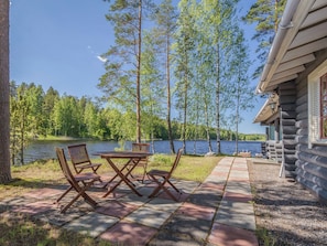 A lakeside cabin with a patio table and chairs, surrounded by trees and a view of the lake. - Aurinkoniemi by Interhome (Mikkeli)